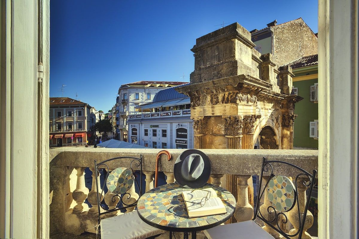A balcony with a view of historic buildings, a tiled table, and a hat.