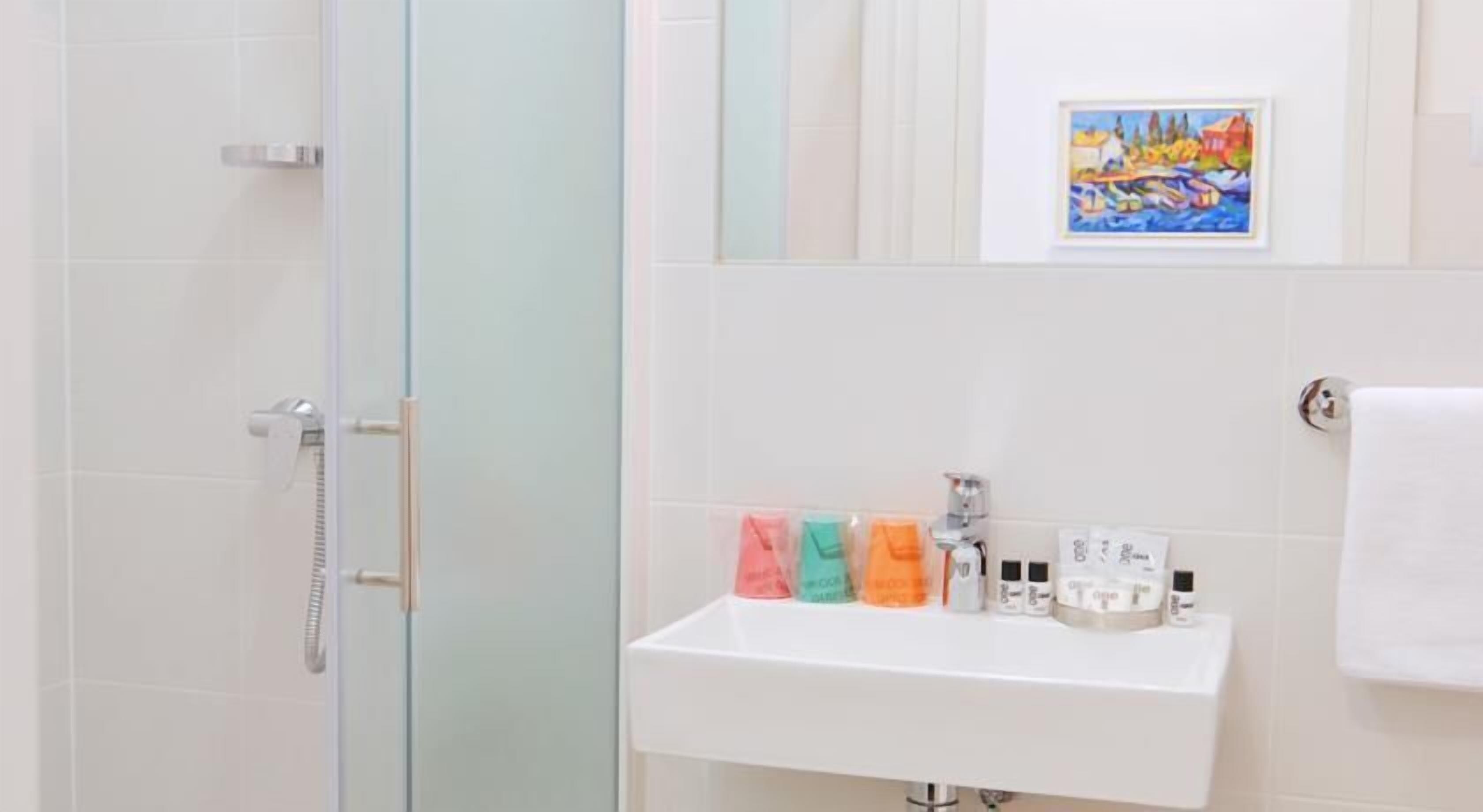 Ein Badezimmer mit Duschabtrennung aus Glas, einem weißen Waschbecken mit Pflegeprodukten und einem gerahmten Gemälde an der Wand.