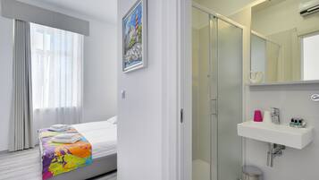 Una habitación de hotel moderna con una cama, ducha y baño con lavabo y espejo.