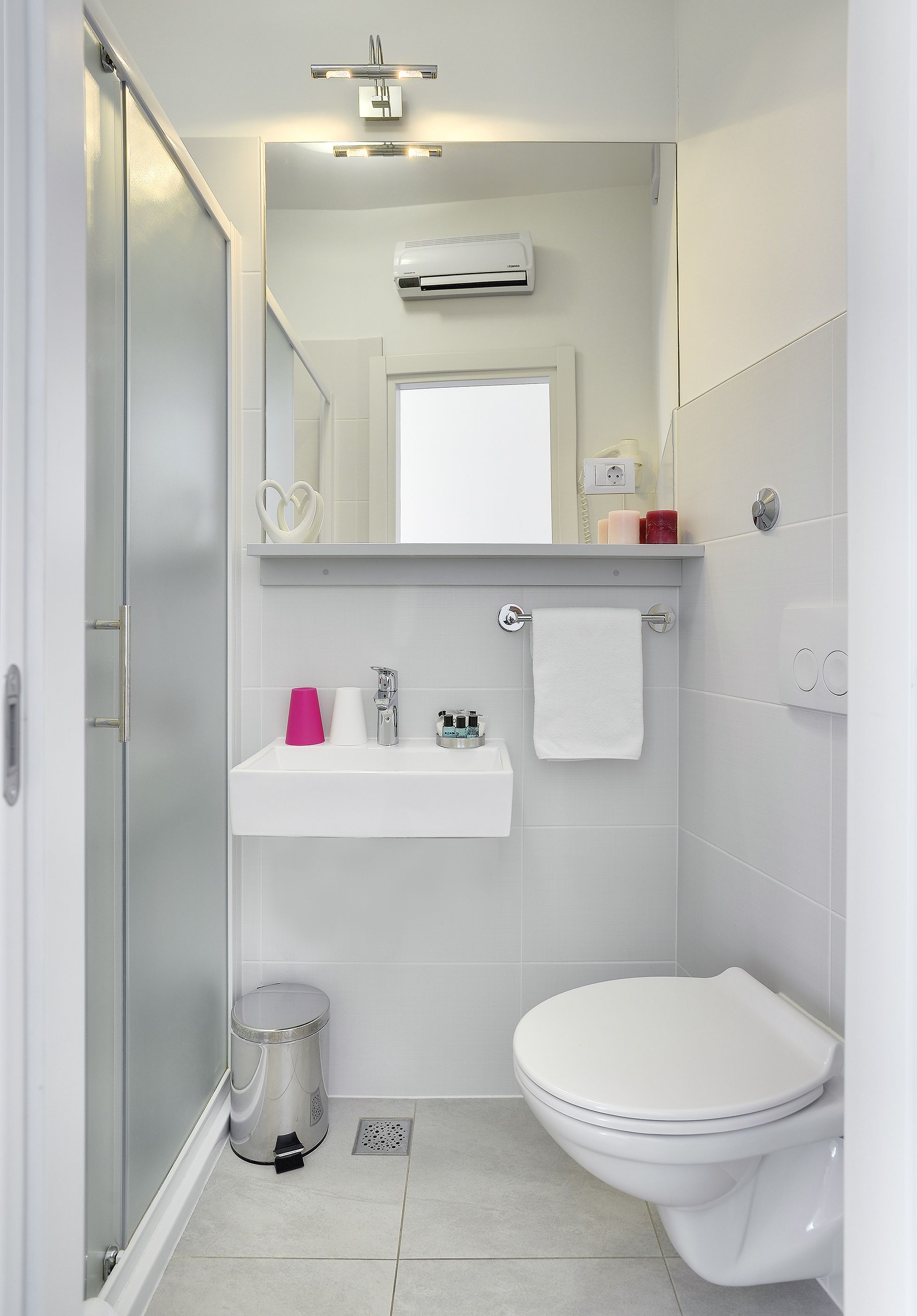 Un baño moderno con cabina de ducha de vidrio, un lavamanos blanco con espejo superior y un inodoro.