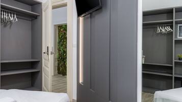 Un dormitorio moderno con cama, televisión montada en la pared y vestidor con estantes y espacio para colgar ropa.