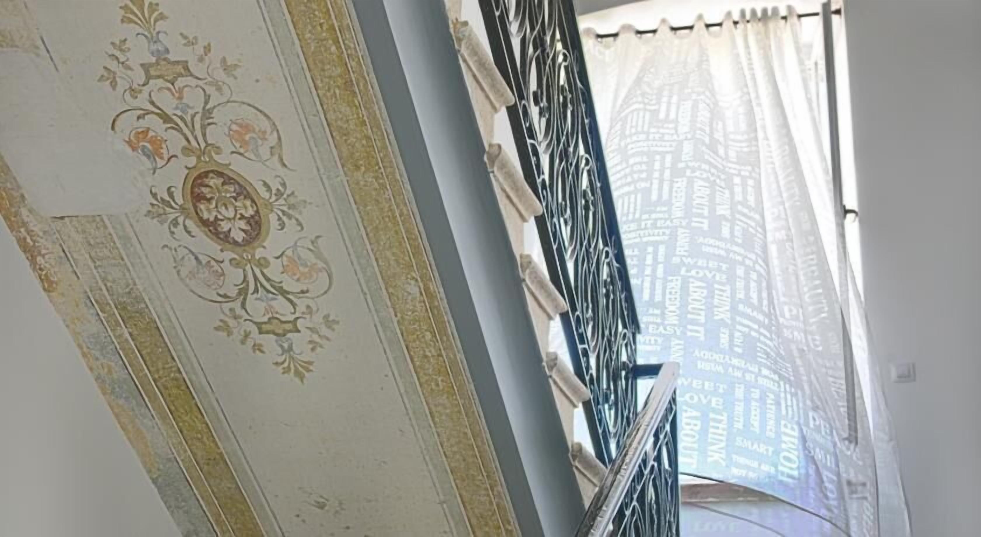 Une pièce ornée de décorations complexes au plafond, une fenêtre avec un rideau à motifs et une rambarde en métal.