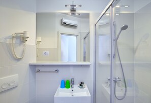 Ein modernes Badezimmer mit Duschkabine aus Glas, einem weißen Waschbecken mit Pflegeprodukten und einem angebrachten Föhn.