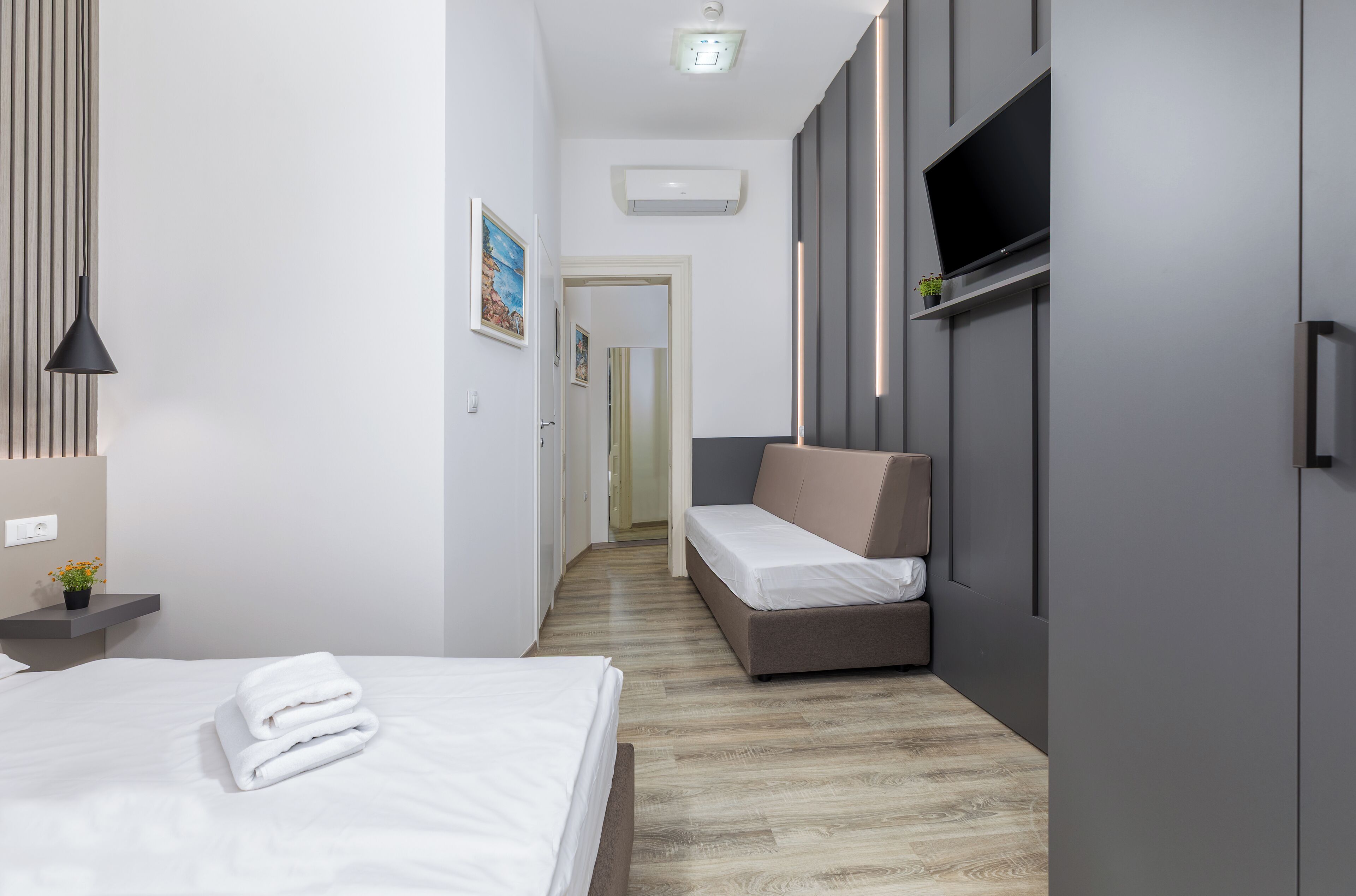 Quarto de hotel moderno com cama, sofá, televisão e armário.