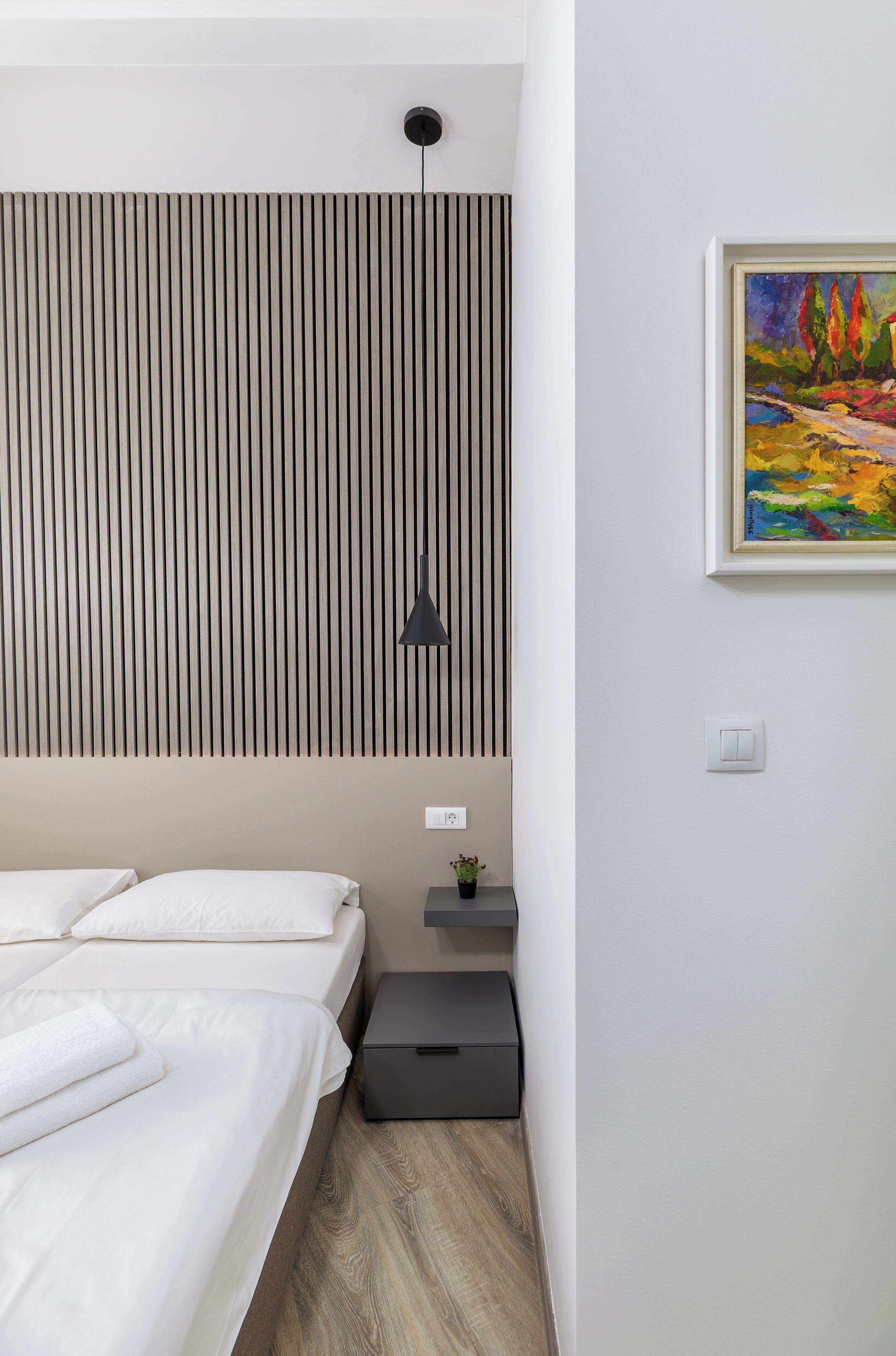 A modern bedroom with a bed, a bedside table, a lamp, and a painting on the wall.
