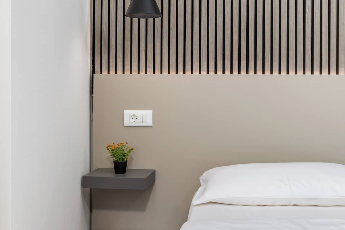 A modern bedroom with a bed, bedside table, and a small shelf with a plant.