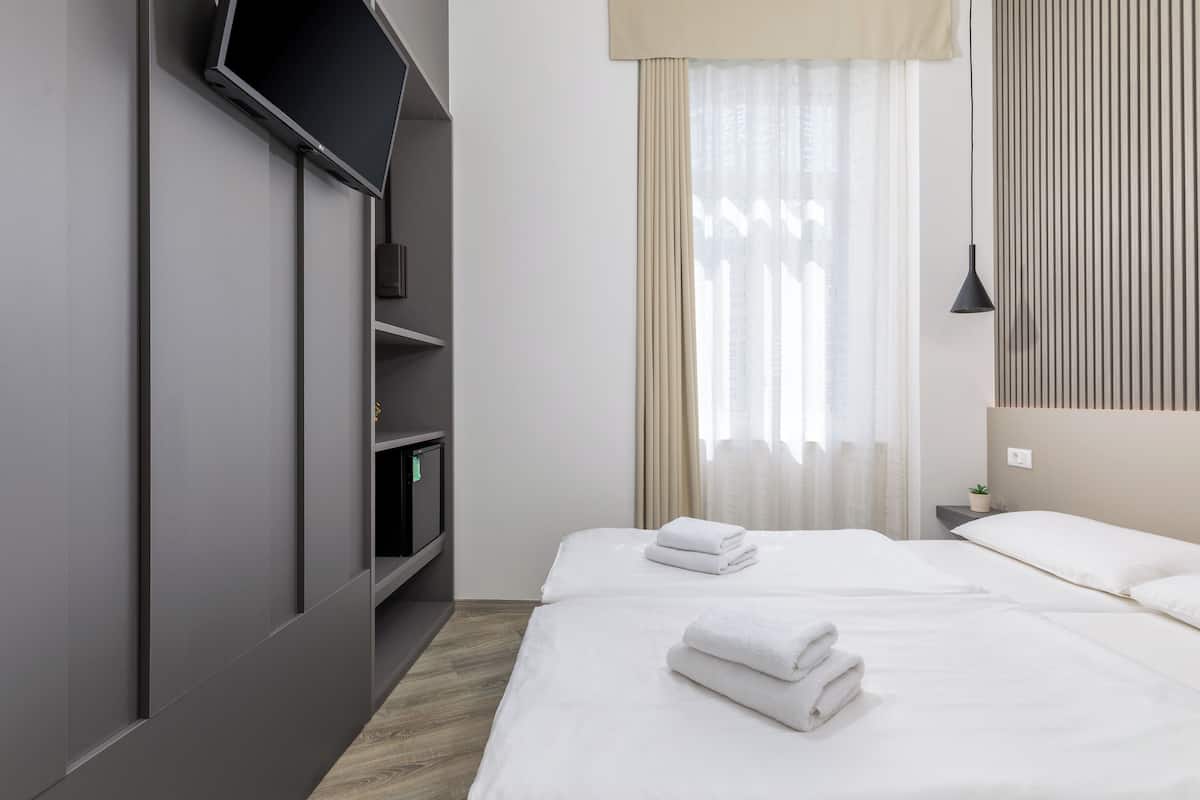A modern hotel room with a flat-screen TV mounted on the wall, a bed with neatly folded white towels, and a bedside table with a lamp.