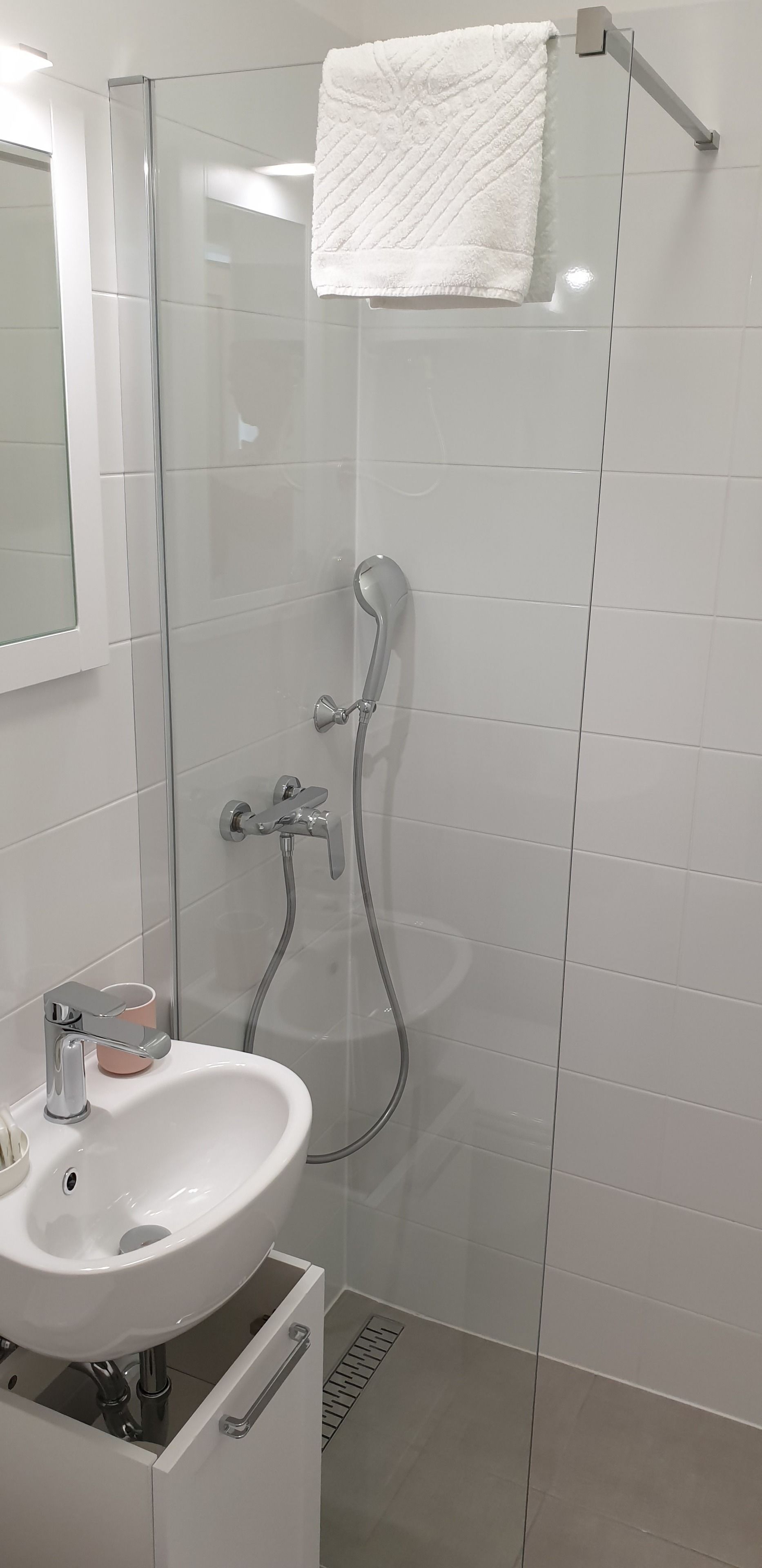 A modern bathroom with a glass-enclosed shower, a white sink, and a cup on the counter.