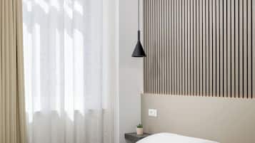 A hotel room with a large bed, two pillows, a bedside table with a lamp, and a wall with vertical lines.
