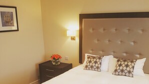 Una habitació d'hotel amb un llit gran, una tauleta de nit amb un ram de flors i un quadre al mur.