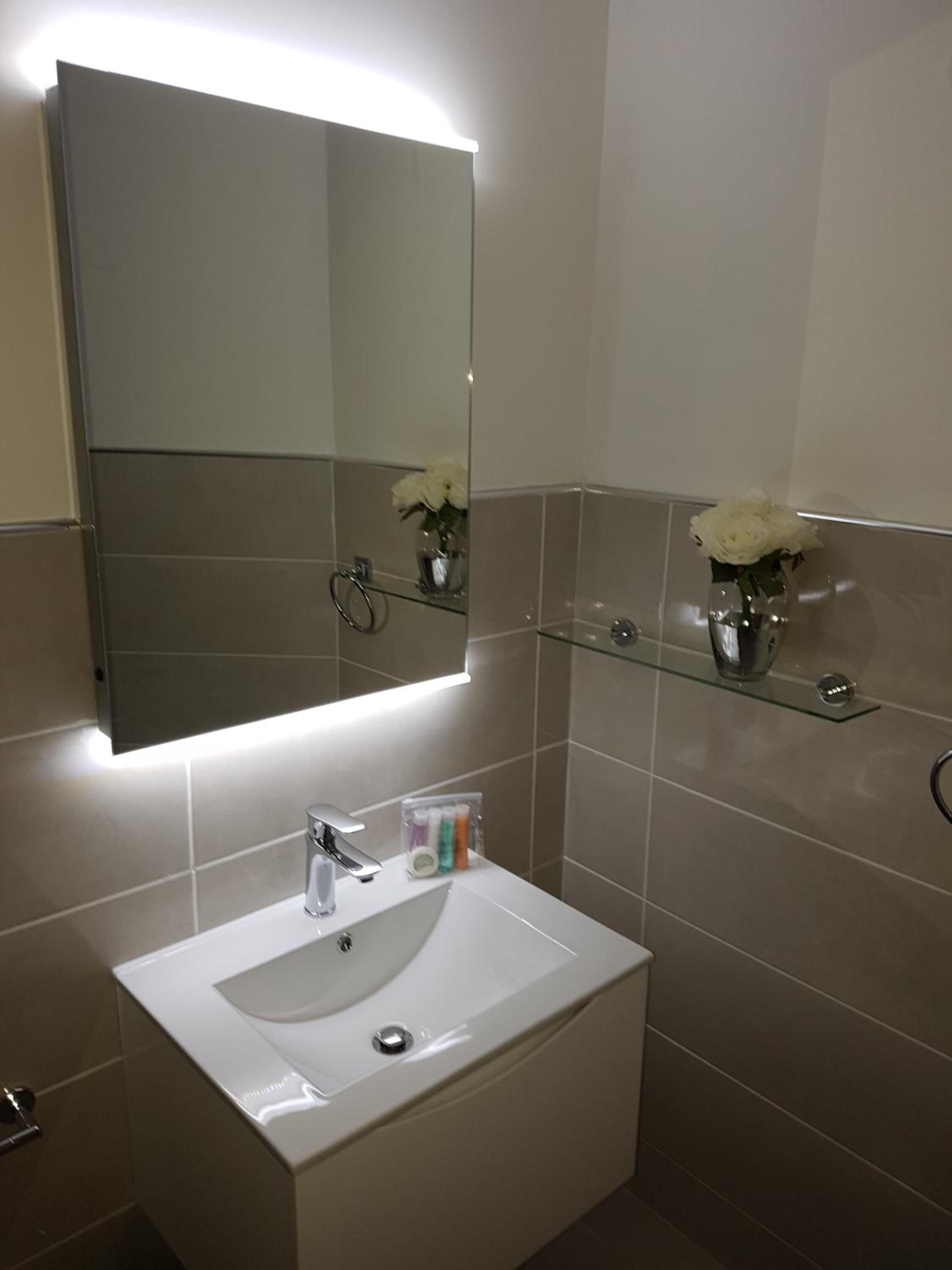 A modern bathroom with a white sink, a mirror, and two glass shelves with white flowers.