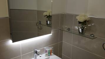 A modern bathroom with a white sink, a mirror, and two glass shelves with white flowers.