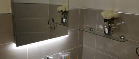 Un baño moderno con un lavamanos blanco, un espejo y dos repisas de vidrio con flores blancas.