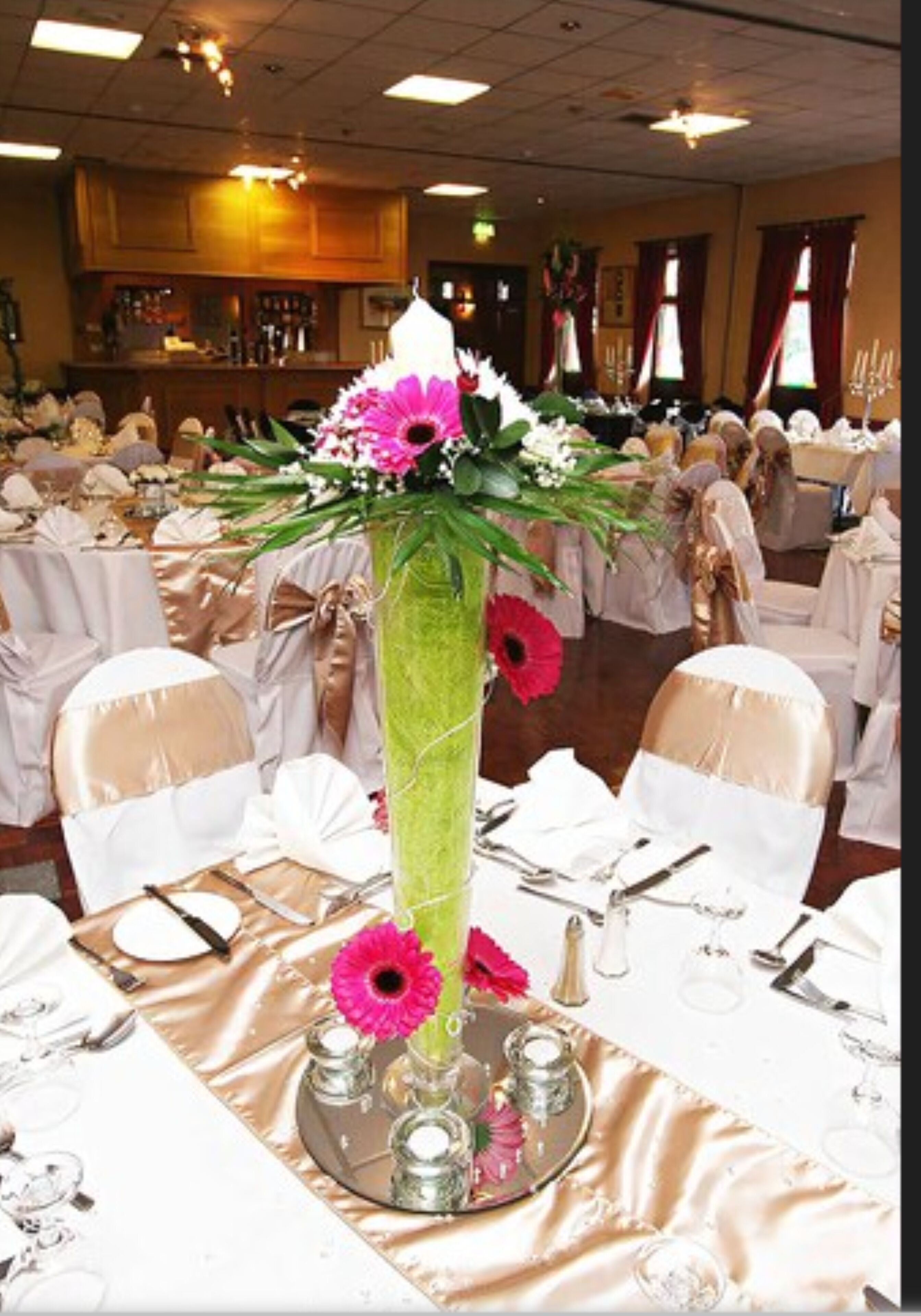 A banquet hall with round tables set for a formal event, featuring a central floral arrangement.
