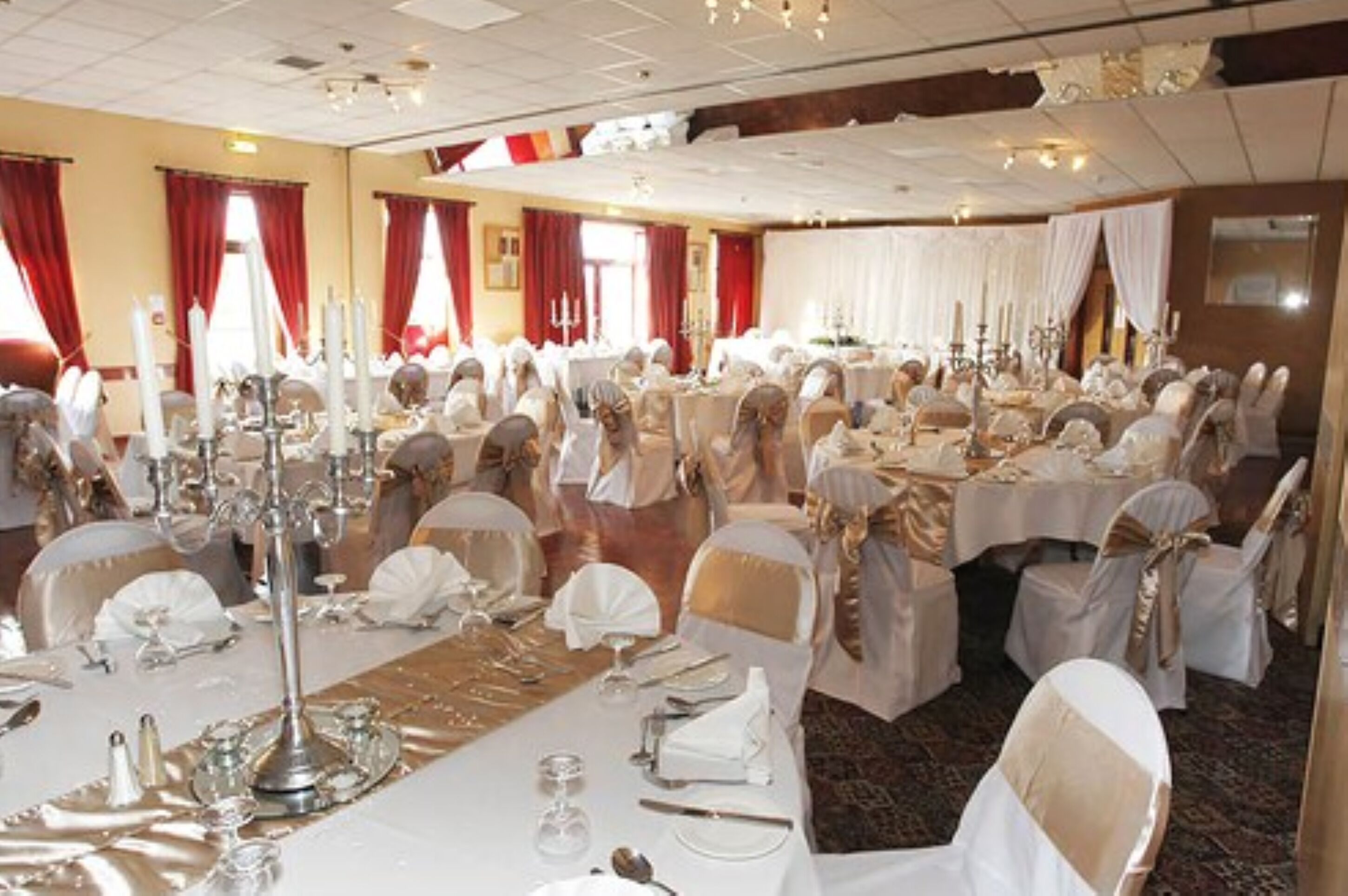 A banquet hall with round tables set for a formal event, featuring white tablecloths and gold sashes on chairs.