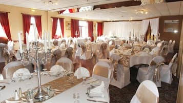 A banquet hall with round tables set for a formal event, featuring white tablecloths and gold sashes on chairs.