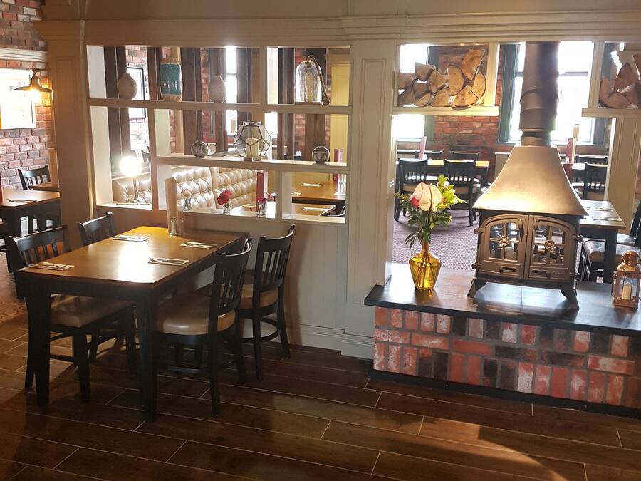 Interior d'un restaurant acollidor amb paret de maó, taules de fusta i una gran làmpada penjant.