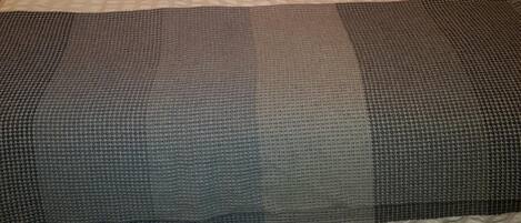 Una cama con cuidada presentación, cabecera tapizada, dos almohadas y una colcha gris y blanca con estampado.