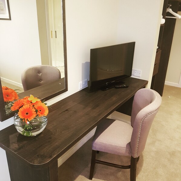 A dark wooden desk with a flat-screen TV, a remote control, and a vase of orange flowers.