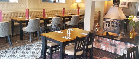 A cozy dining area with a fireplace, wooden tables, and cushioned chairs.