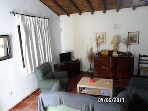 A living room with a television, a green armchair, a wooden coffee table, and a cabinet with decorative items. - La Alberguería (Canamero)