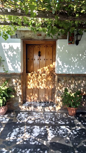 A wooden door with a keyhole, surrounded by stone walls and potted plants. - La Alberguería (Canamero)