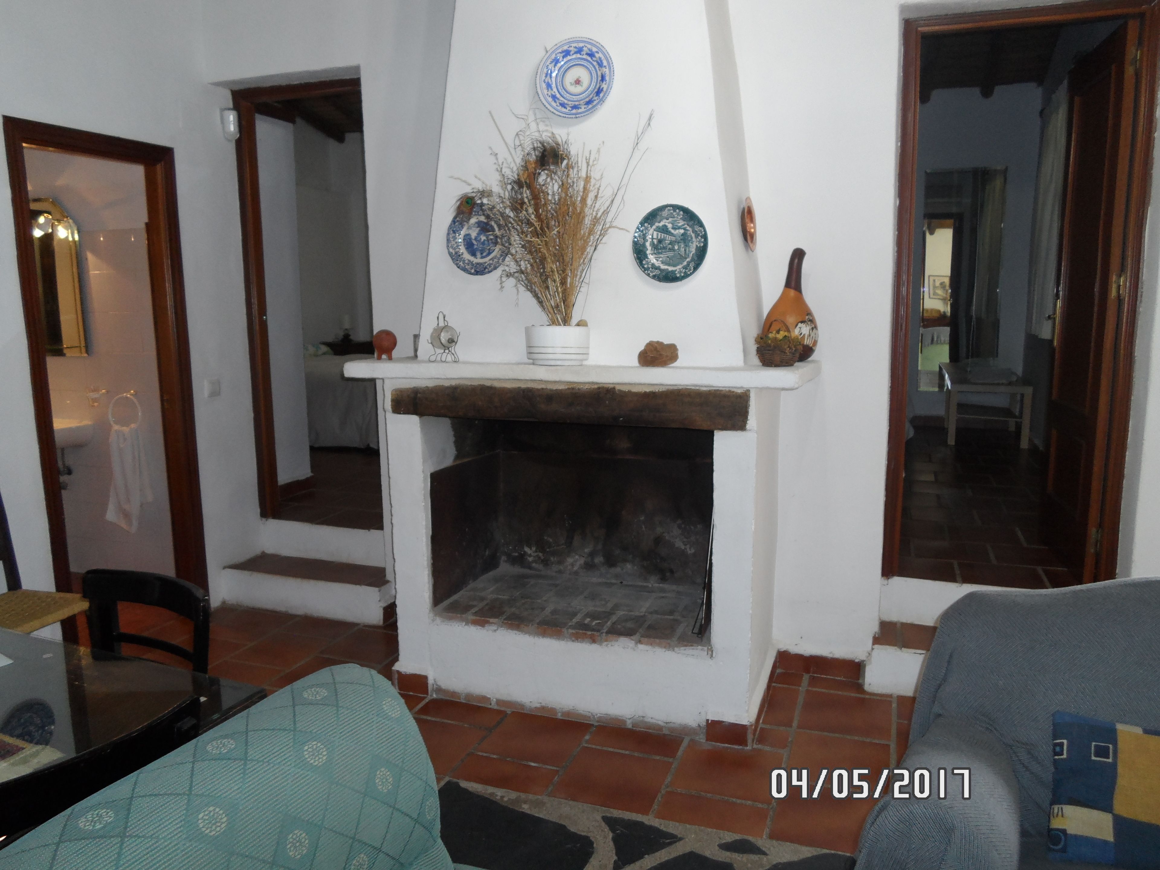 Una sala de estar con chimenea, una mesa de comedor y un sofá. Hay platos decorativos y un jarrón sobre la repisa.