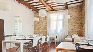 Comedor con mesas y sillas blancas, paredes de piedra y vigas de madera.