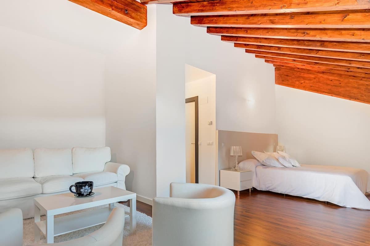 Un dormitorio moderno con un sofá blanco, una mesita con una taza de café, un sillón blanco y una cama con ropa de cama blanca.
