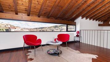 A modern room with a wooden ceiling, two red chairs, a small table, and a view of a rural landscape through a large window.