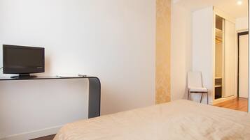 A bedroom with a bed, a TV on a stand, a chair, and a wardrobe.