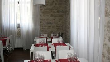 Un comedor con mesas dispuestas para cuatro, cada una con copas de vino y cubiertos. La habitación tiene paredes blancas y una pared de acento de piedra.