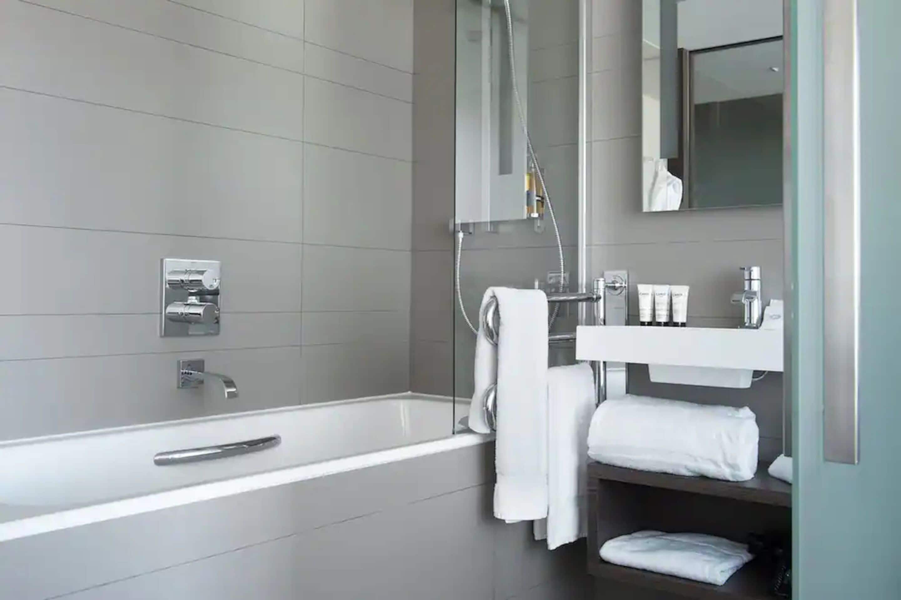 Un baño moderno con una bañera grande, cabina de ducha con mampara de vidrio, tocador con artículos de aseo y un espejo.