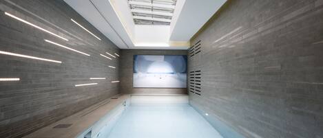 A modern indoor swimming pool with a skylight, tiled walls, and a view of the sky.