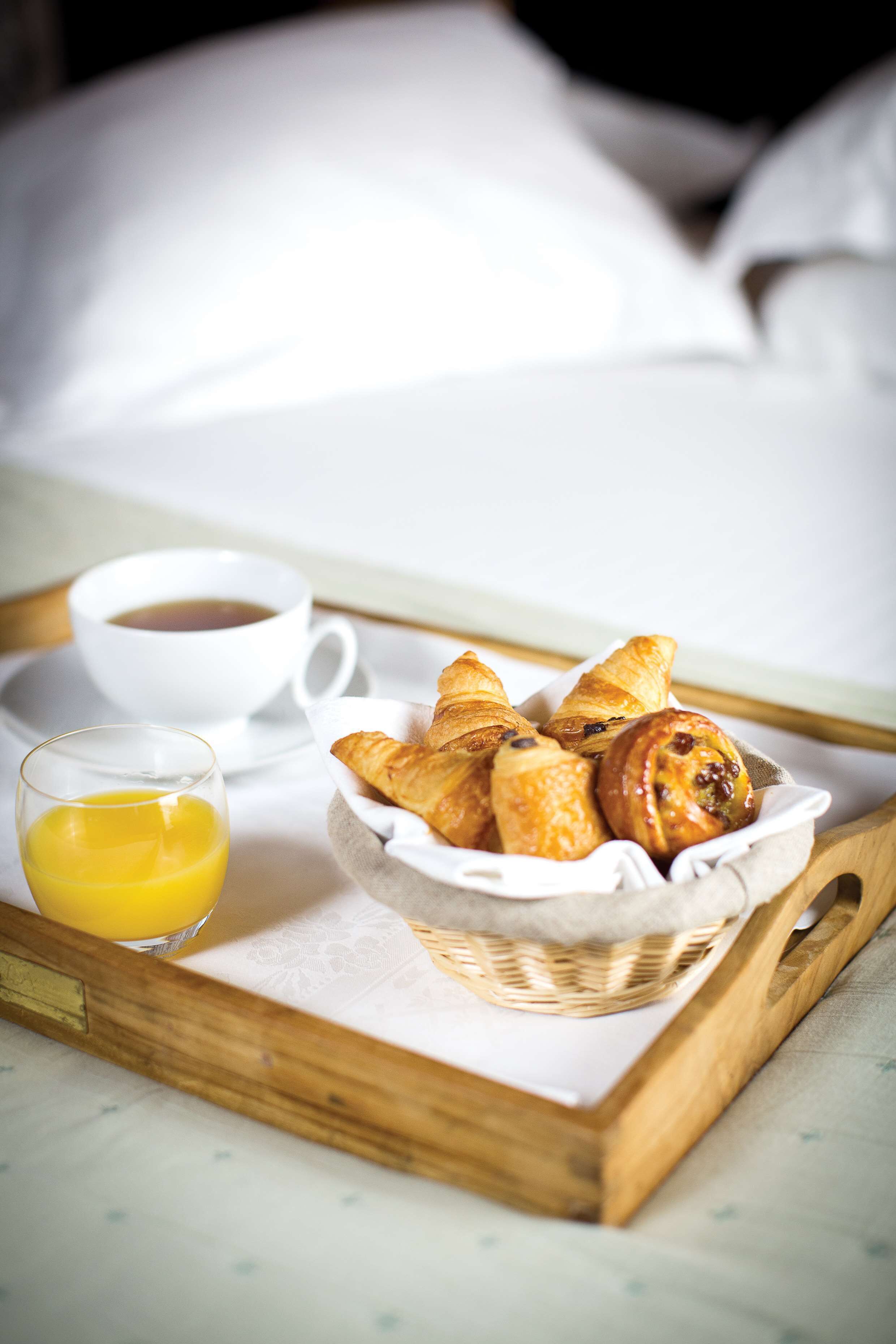 A tray with croissants, a cup of coffee, and a glass of orange juice on a bed.