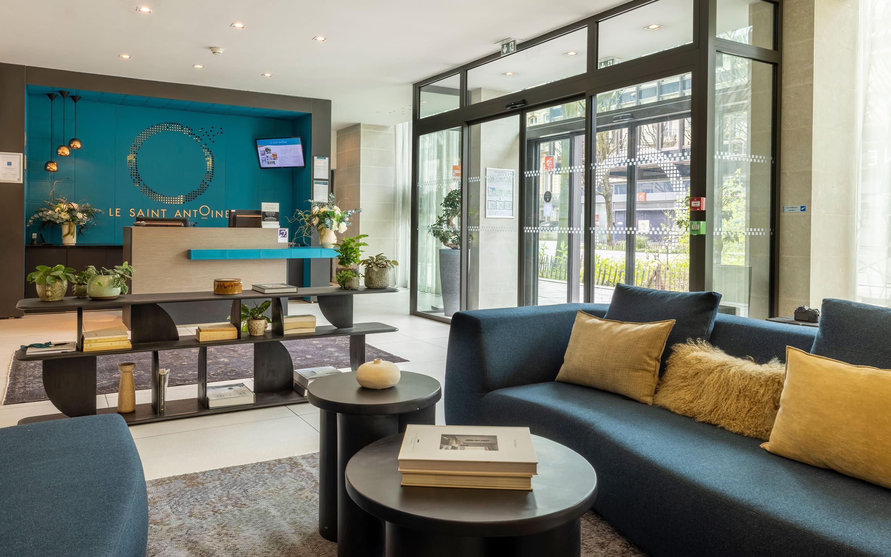 A modern hotel lobby with a reception desk, seating area, and large windows.