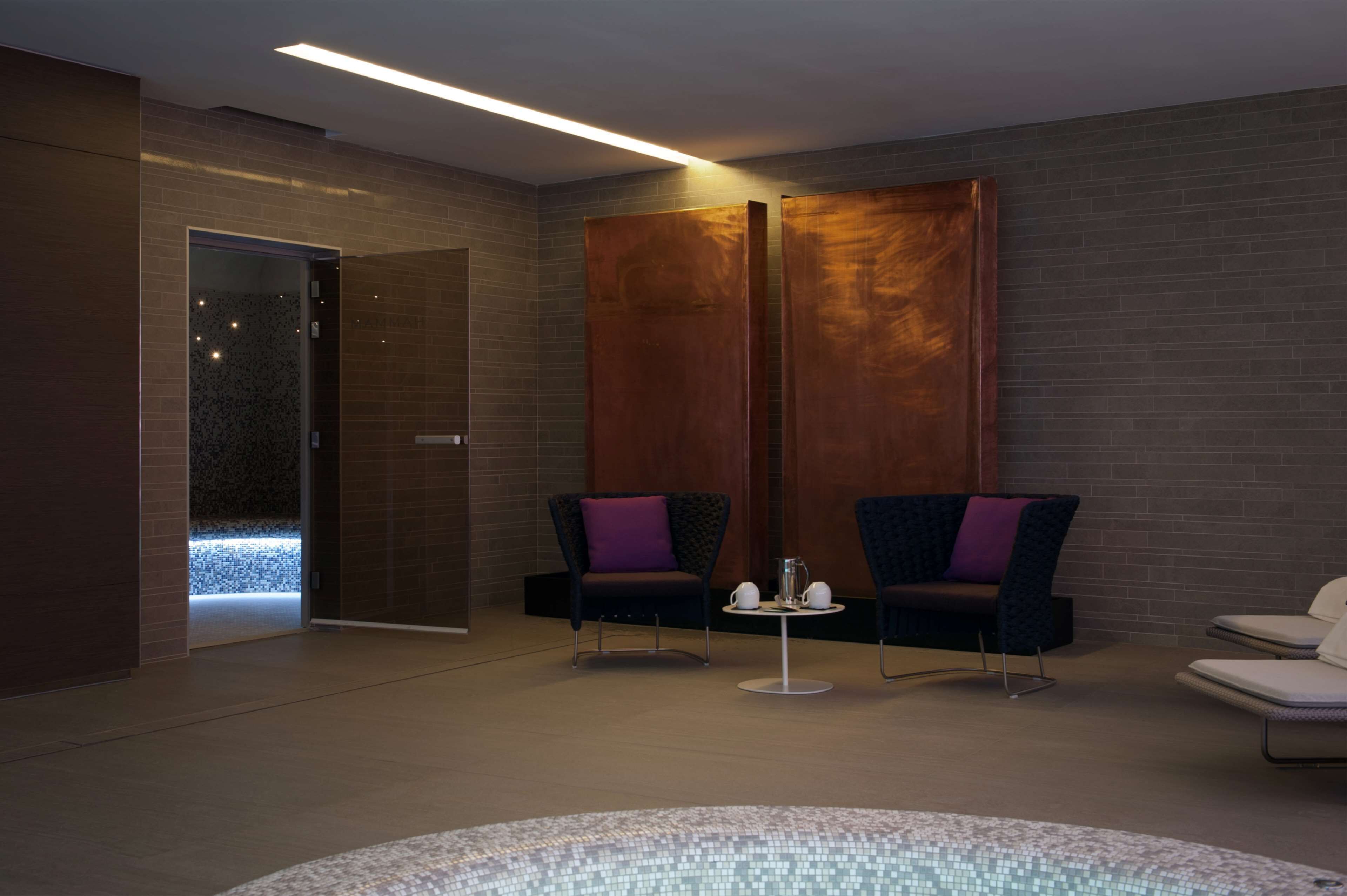 Un moderno cuarto de spa con dos sillones oscuros, una mesita con una tetera y un gran panel de pared de madera.