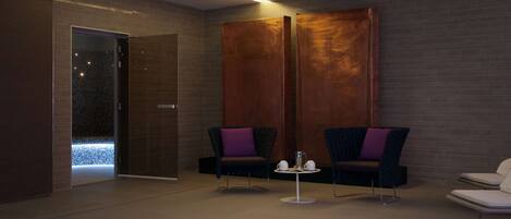 A modern spa room with two dark armchairs, a small table with a teapot, and a large wooden panel wall.