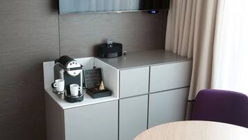 A hotel room with a coffee machine, two cups, and a tray with a coffee pot and a small item on a cabinet.