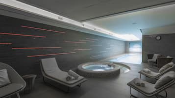 A modern indoor spa with a heated stone bath, lounge chairs, and a wall with red LED lighting.