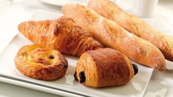 A breakfast setting with croissants, a muffin, and a cup of coffee on a white table.