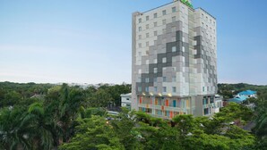 A modern hotel with a multi-story structure, featuring a prominent green sign at the top. - ibis Styles Makassar Sam Ratulangi (Makassar)