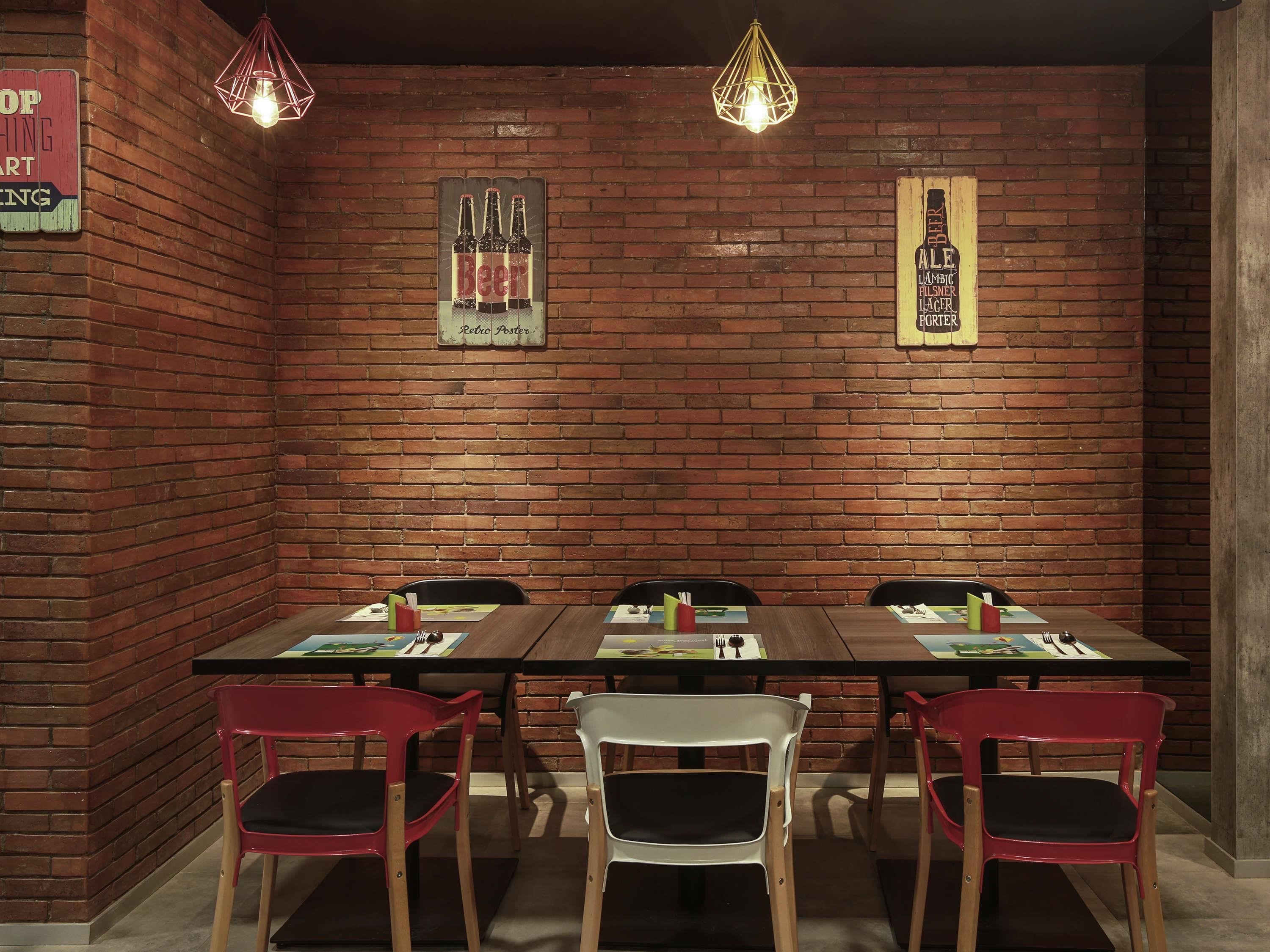 A brick-walled room with a long table and chairs, two retro posters, and hanging light fixtures.