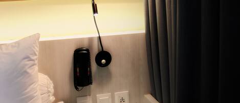 Habitación de hotel con cama, mesita de noche, lámpara, teléfono y pared con rayas horizontales.
