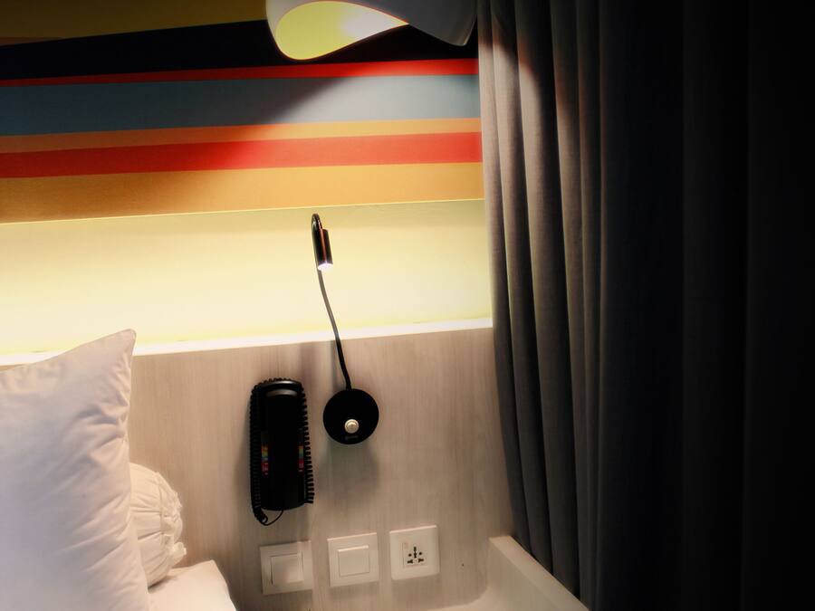 A hotel room with a bed, a bedside table, a lamp, a phone, and a wall with horizontal stripes.
