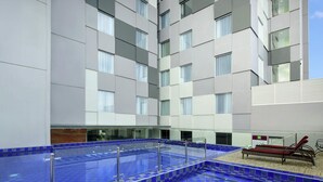 A modern hotel with a large indoor swimming pool, a lounge area with red chairs, and a multi-story building with large windows. - ibis Styles Makassar Sam Ratulangi (Makassar)