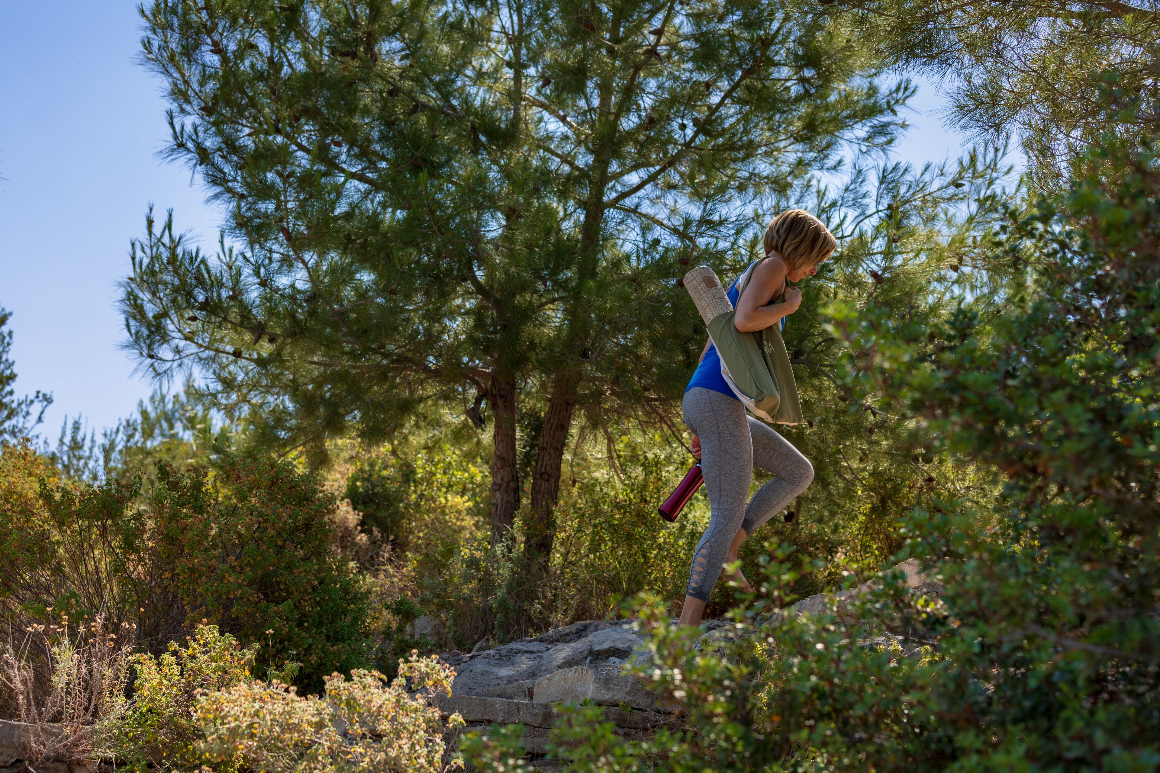 Una persona caminando en un área boscosa con árboles y rocas.