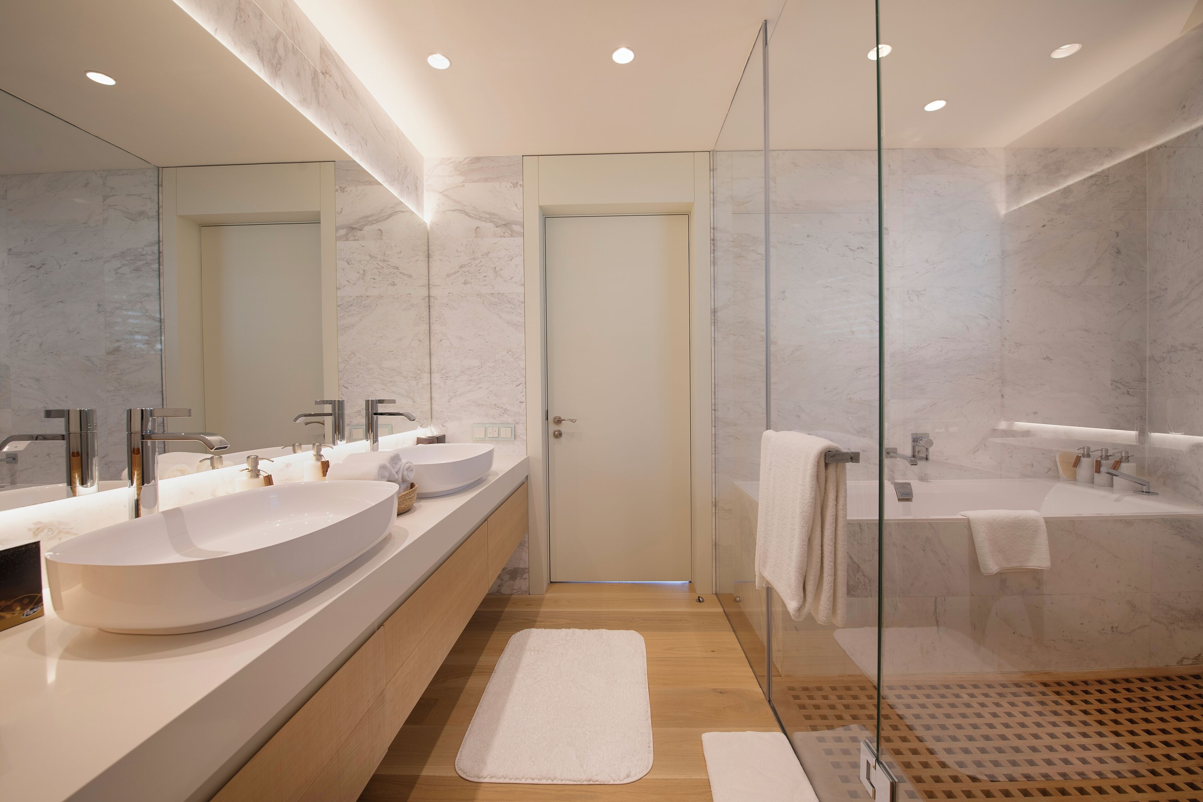 A modern bathroom with a large white sink, a glass-enclosed shower, and a wooden floor.