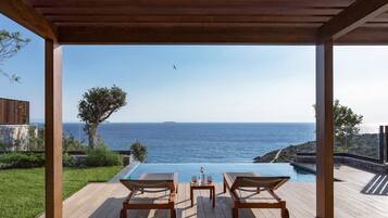 A wooden deck with a pool and lounge chairs overlooking the sea.