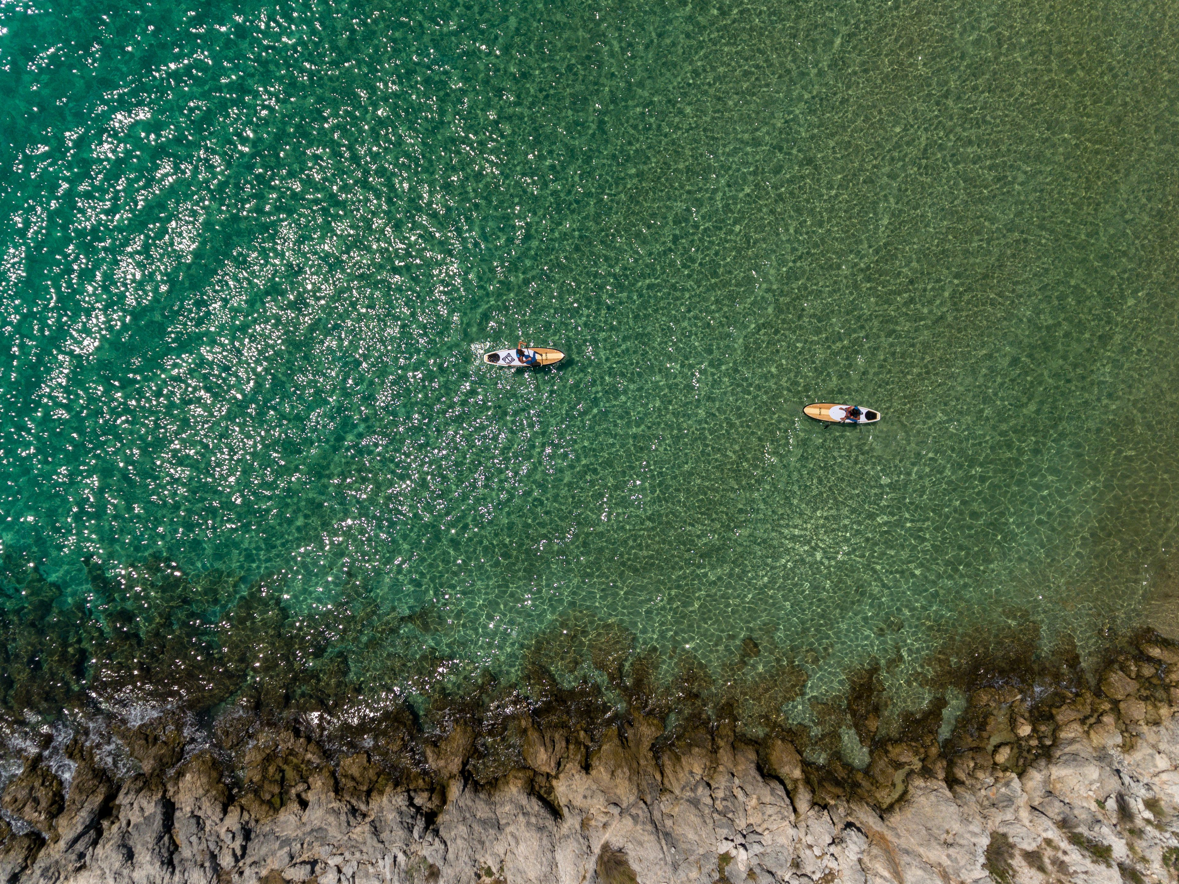 An aerial view of a beach with two boats and rocky shoreline.